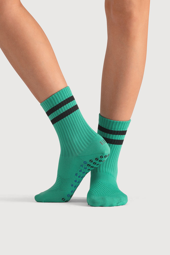 Green socks with black stripes worn by a person on a light gray background