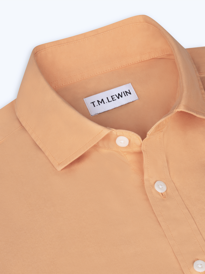 Close-up of a apricot yellow shirt with a T.M. Lewin label on a white background